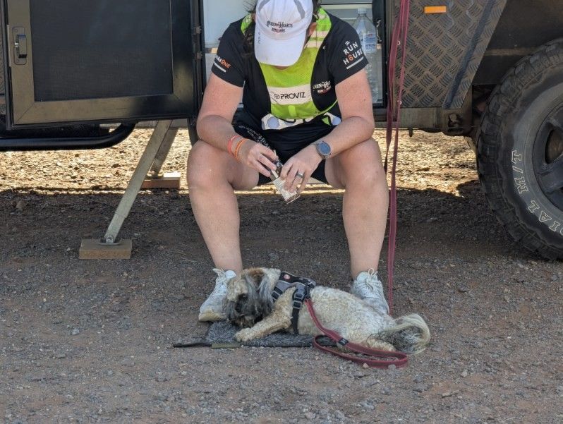 Dawn resting in the shade of the support trailer with her dog on a hard day