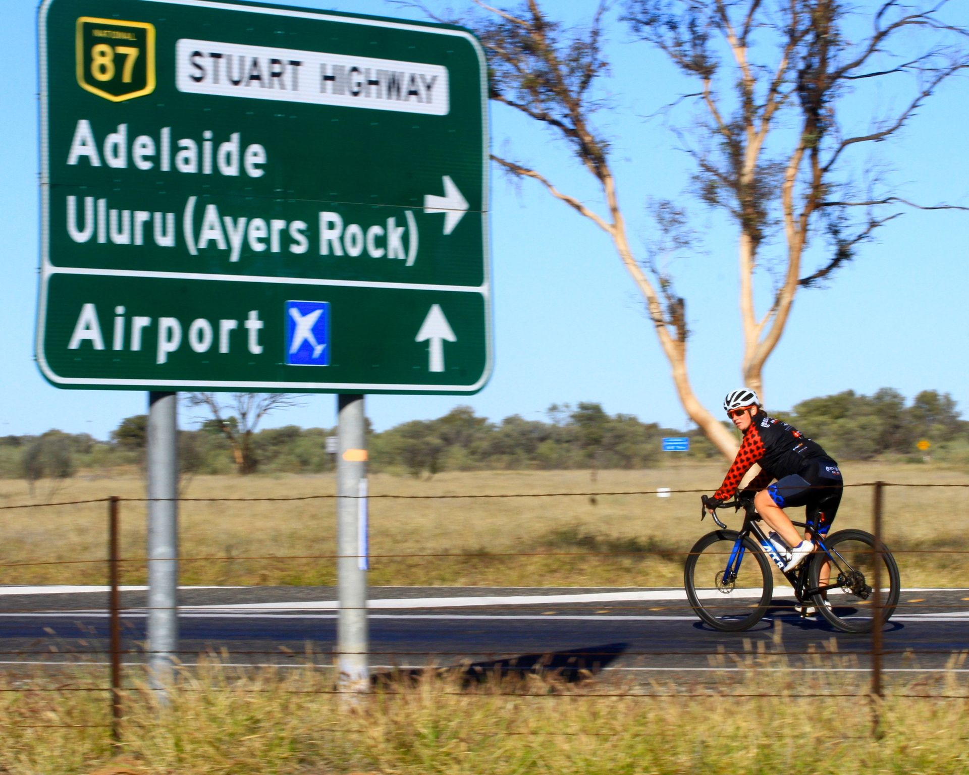 Dawn cycling past the Stuart Highway sign pointing to Adelaide and Uluru